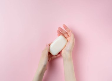 Kadının elleri pastel pembe arka planda sabun tutuyor. Üst manzara, düz uzanma.