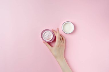 Pastel pembe arka planda bir kadının el kremi kavanozu.