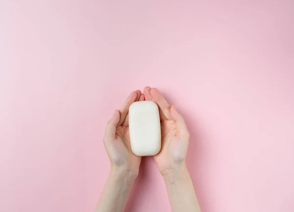 Kadının elleri pastel pembe arka planda sabun tutuyor. Üst manzara, düz uzanma.