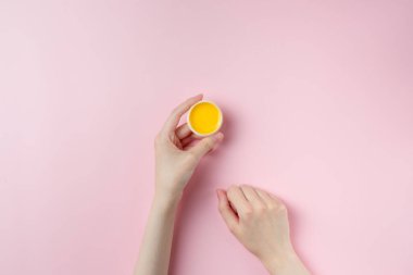 Pastel pembe arka planda bir kadının el kremi kavanozu.