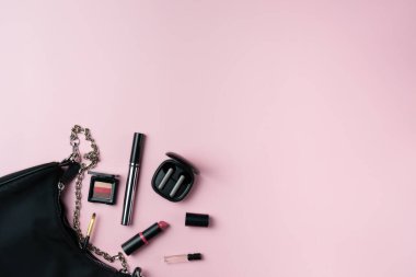 Kadınların eşyaları pembe arka planda bir çantadan düşerler.