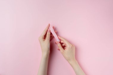Kadının elleri pembe arka planda küçük pembe bir tüp tutuyor.