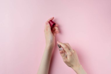 Kadın elleri pastel pembe arka planda parfüm sıkıyor.