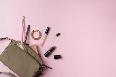 Kadınların eşyaları pembe arka planda bir çantadan düşerler.