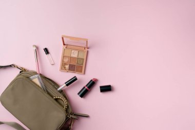 Kadınların eşyaları pembe arka planda bir çantadan düşerler.