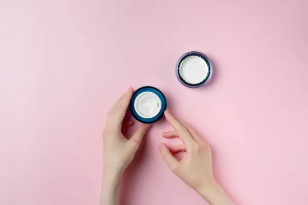Pastel pembe arka planda bir kadının el kremi kavanozu.
