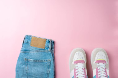 Pembe arka planda kot pantolon ve spor ayakkabılar. Gündelik sokak tarzı, üst bakış açısı, düz yatış.