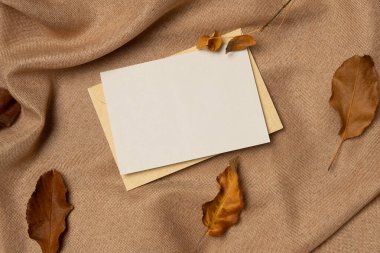 Yukarıdan gelen kumaş arkaplanında yapraklar olan boş beyaz kağıt listesi. Sonbahar konsepti. Boşluğu kopyala