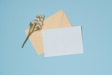 Yukarıdan mavi arka planda çiçek olan zarf ve boş beyaz kağıt listesi. Boşluğu kopyala