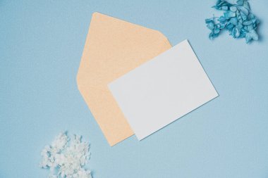 Zarflı boş beyaz kağıt listesi ve yukarıdan mavi arka planda çiçekler. Boşluğu kopyala