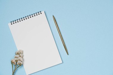 Yukarıdan mavi arka planda kalem ve çiçekli boş bir defter. Boşluğu kopyala