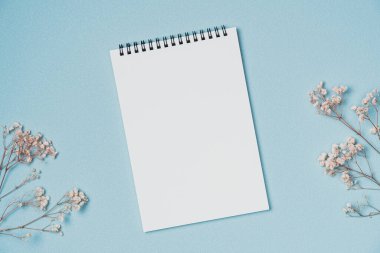 Mavi arka planda çiçekli boş bir defter. Boşluğu kopyala
