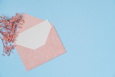 Yukarıdan mavi arka planda çiçek olan zarf ve boş beyaz kağıt listesi. Boşluğu kopyala