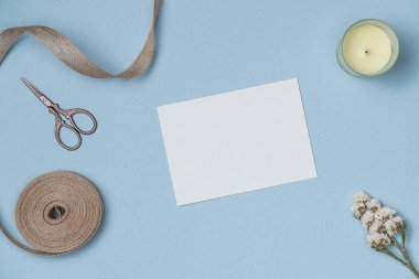 Yukarıdan mavi arka planda kurdele, makas, mum ve çiçekli beyaz kağıt listesi. Boşluğu kopyala