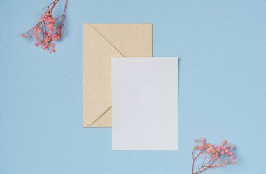 Yukarıdan mavi arka planda çiçek olan zarf ve kağıt boş bir sayfa. Metin için boşluk