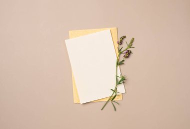 Yukarıdan gelen bej arka planda çiçek olan zarf ve kağıt boş çarşaf. Metin için boşluk
