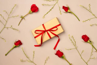 Yukarıdan bej arka planda kırmızı güllerden oluşan bir hediye kutusu. Düz yatış, üst görünüm.