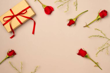 Bej arka planda hediye kutusu olan kırmızı güller çerçevesi. Düz yerde, üst tarafta. Boşluğu kopyala