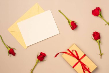 Üzerinde kırmızı güller ve yukarıdan gelen bej arka planda hediye kutusu olan kâğıt boş bir sayfa. Tebrik kartı. Metin için boşluk