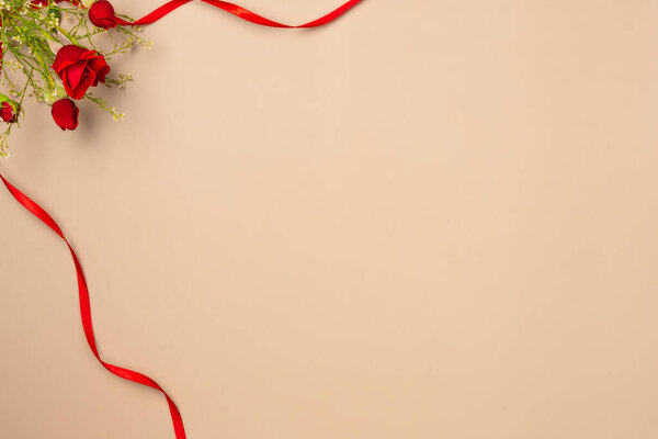 Beige background with red roses and ribbon. Flat lay, top view. Copy space