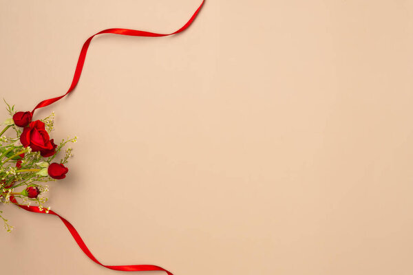 Beige background with red roses and ribbon. Flat lay, top view. Copy space