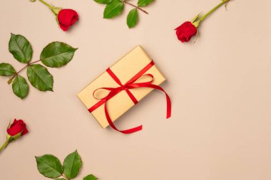 Bej arka planda hediye kutusu olan kırmızı güller. Düz yerde, üst tarafta. Boşluğu kopyala