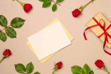 Kırmızı gül çerçeveli kağıt boş sayfa ve yukarıdan bej arka planda hediye kutusu. Tebrik kartı. Metin için boşluk