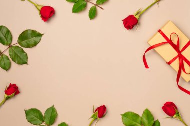 Bej arka planda hediye kutusu olan kırmızı güller çerçevesi. Düz yerde, üst tarafta. Boşluğu kopyala
