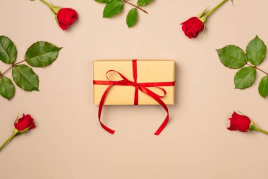 Yukarıdan bej arka planda kırmızı güllerden oluşan bir hediye kutusu. Düz yatış, üst görünüm.