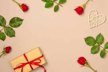 Kırmızı güller çerçevesi, hediye kutusu ve bej arka planda kalp. Düz yerde, üst tarafta. Boşluğu kopyala