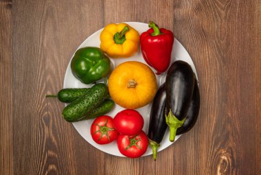 Kabaklar, patlıcanlar, salatalıklar, domatesler ve farklı renkte biberler tabakta. Sonbahar hasadı. Üst manzara, düz uzanma