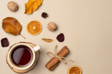 Bir fincan çay, yaprak, fındık, koni, kurutulmuş meyve, bej arka planda tarçın çubukları ile sonbahar kompozisyonu. Üst manzara, düz uzanma