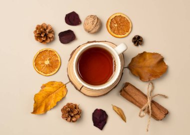 Bir fincan çay, yaprak, fındık, koni, kurutulmuş meyve, bej arka planda tarçın çubukları ile sonbahar kompozisyonu. Üst manzara, düz uzanma