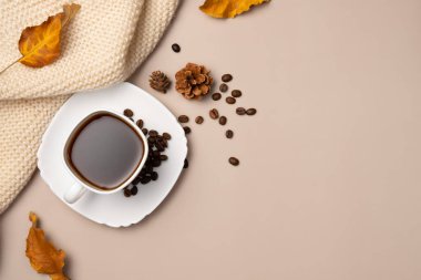 Bir fincan kahve, kahve çekirdekleri, koniler, yapraklar ve bej arka planda eşarp. Sonbahar kompozisyonu. Uzayı kopyala Düz yatış, üst görünüm