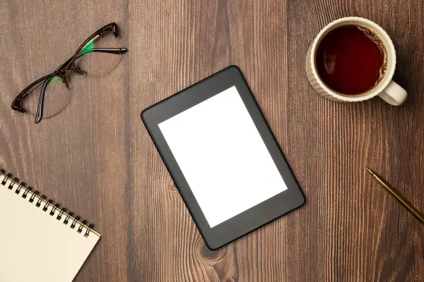E-kitaplar, defter, bardaklar ve yukarıdan ahşap arka planda bir fincan çay. Düz yatış, üst görünüm.