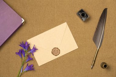 Kalem, mürekkep, kitap ve çiçeklerle kaplı zarf yukarıdan geliyor. Eski tarz. Düz yatış, üst görünüm.