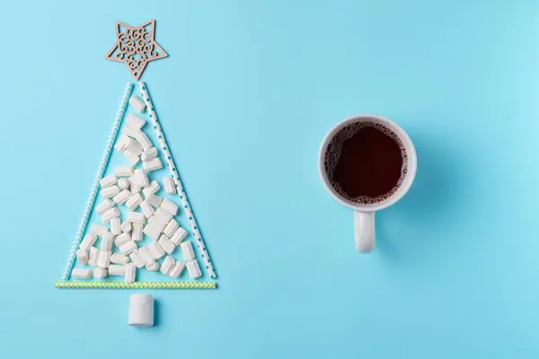 Yukarıdan mavi arka planda dekoratif lokum ağacı olan bir fincan sıcak çikolata. Noel konsepti. Düz yatış, üst görünüm.
