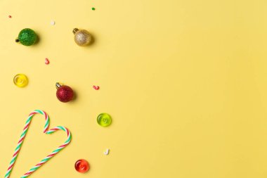 Noel kompozisyonu, yukarıdan gelen sarı arka planda şeker ve toplar. Düz yerde, üst tarafta. Boşluğu kopyala