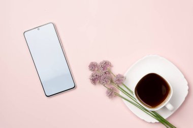 Boş akıllı telefon ekranı, pembe arka planda çiçekli bir kupa kahve. Düz yatış, üst görünüm.