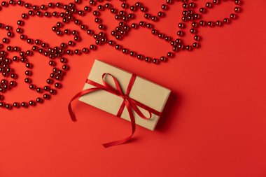 Kırmızı arkaplan, boncuklar ve hediye kutusu. Düz yatış, üst görünüm.