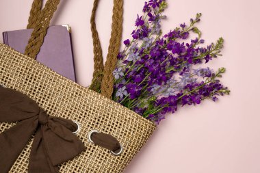 Kitap ve çiçekler pembe arka planda bir çöp torbasında. Düz yatış, üst görünüm.