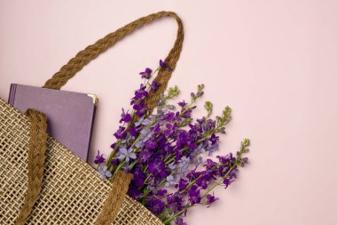 Kitap ve çiçekler pembe arka planda bir çöp torbasında. Düz yatış, üst görünüm.