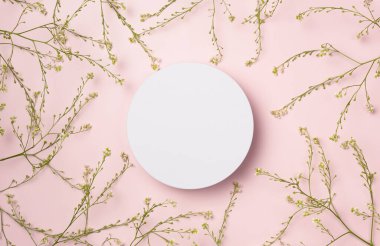 Beyaz yuvarlak podyum, pembe arka planda çiçek çerçeveli kaide ürünü. Düz yatış, üst görünüm.