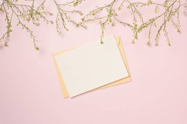 Kağıt boş, pembe arka planda çiçekler var. Düz yatış, üst görünüm.