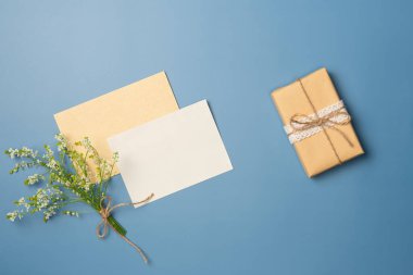 Kağıt boş çarşaf, çiçek buketi ve mavi arka planda hediye kutusu. Düz yatış, üst görünüm.