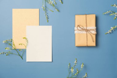 Kağıt boş çarşaf, çiçek buketi ve mavi arka planda hediye kutusu. Düz yatış, üst görünüm.