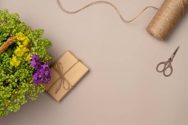 Hediye kutusunda çiçekler, iplik, bej arka planda makas. Düz yatış, üst görünüm.