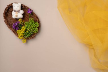 Bej arka planda sarı tül kumaş desenli sepetli ayıcıklı çiçekler. Düz yatış, üst görünüm.