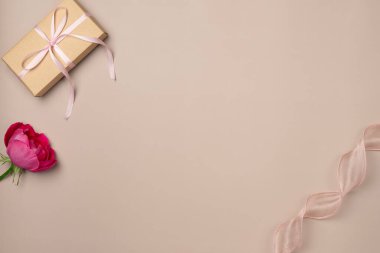 Hediye kutusu, bej arka planda kurdeleli gül. Düz yerde, üst tarafta. Boşluğu kopyala