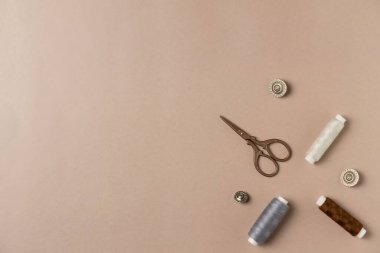 Bej arka planda aksesuarlar dikiyorum. İplik, makas ve düğmeler. Düz yerde, üst tarafta. Boşluğu kopyala